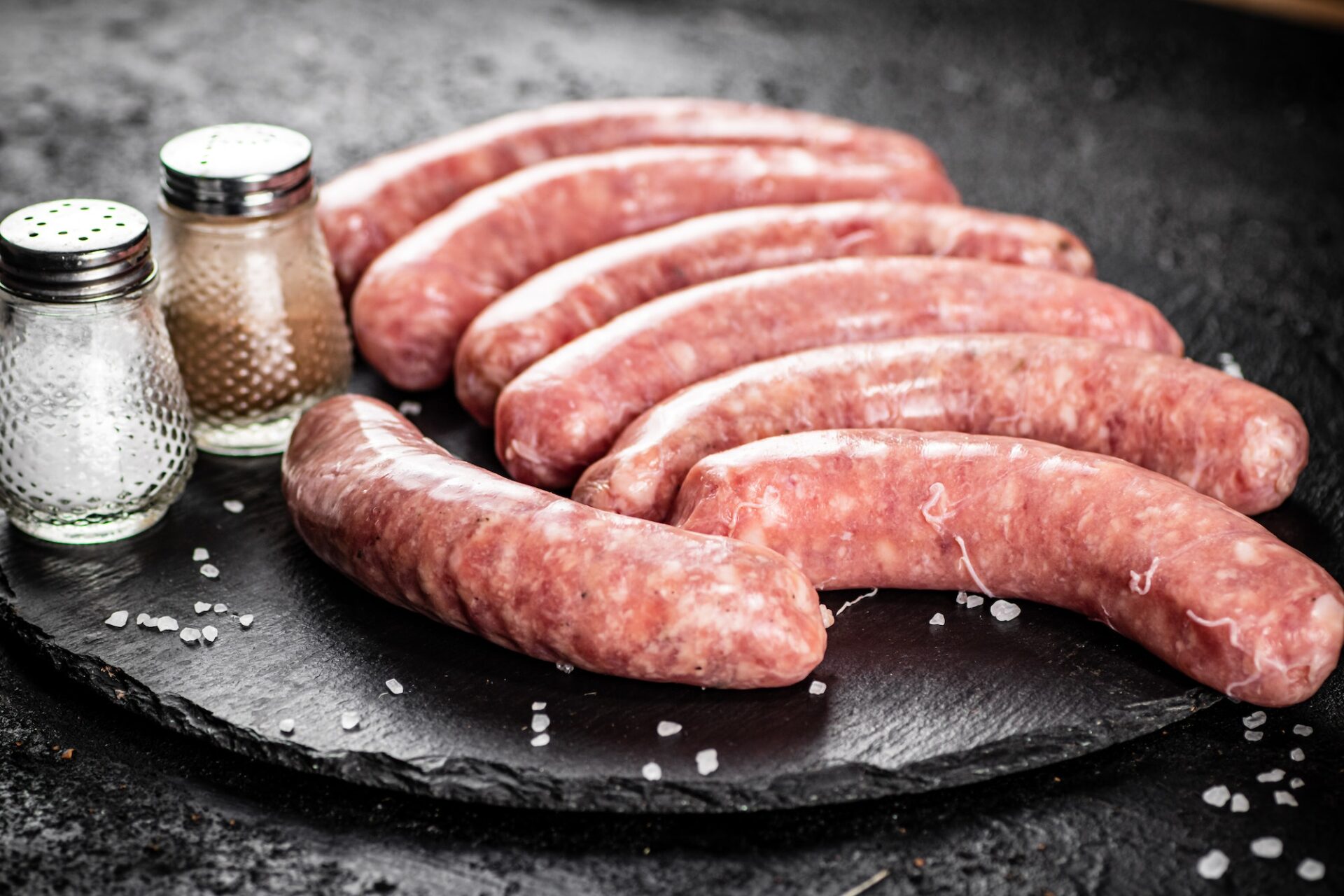 Raw sausages on a stone board with spices.